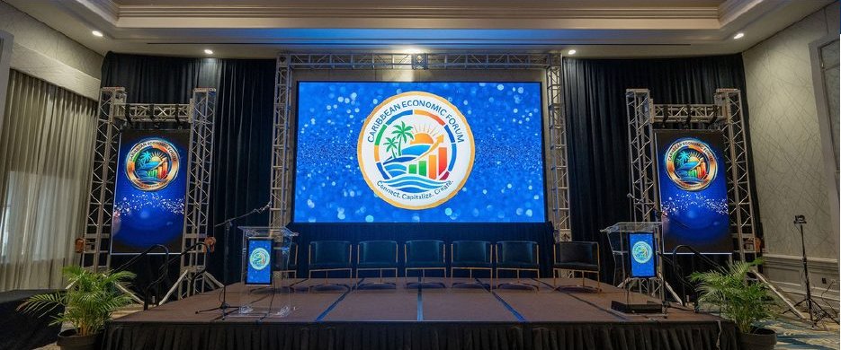 The Caribbean Economic Forum 2026 main stage, its gold-ring logo on the central LED screen and both side towers